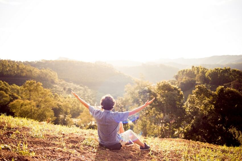 man sitting on the ground outside with his arms up in the air, admiring the beauty of nature