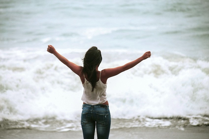 woman facing the ocean with her arms raised
