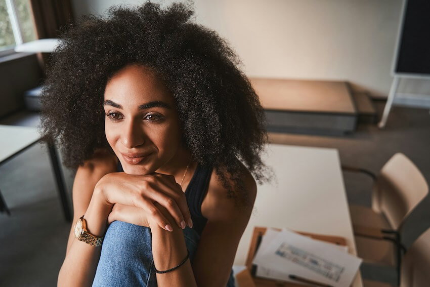 smiling woman resting her head on her hands, looking hopeful