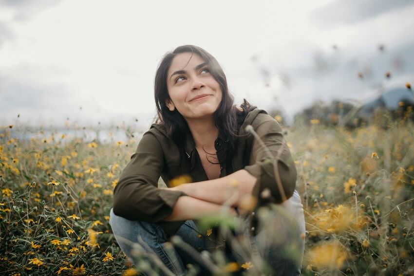 smiling woman sitting in a field of wildflowers looking up at the sky