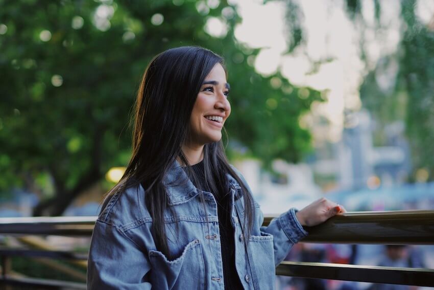 smiling woman standing next to a fence while admiring the view