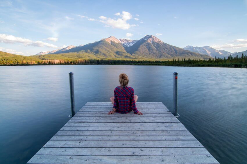 woman sitting at the end of a dock looking over a tranquil blue lake