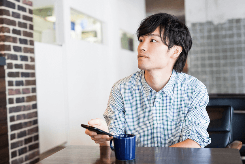 Young man at a café pausing to look up from his phone, noticing the people around him — the first step of the Cherish List™ gratitude practice