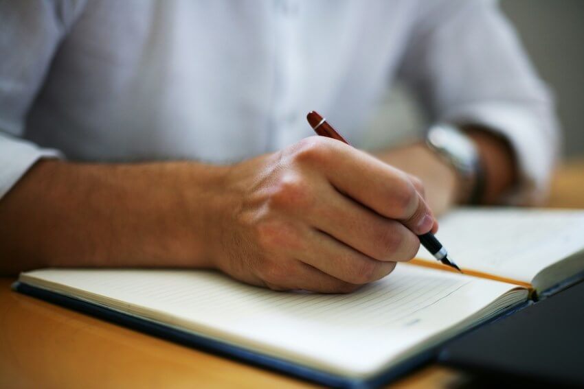 man's hand holding a pen, lingering over a gratitude journal