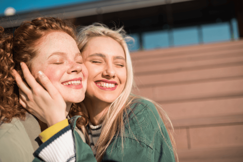 Two young women laughing and embracing in the sunshine, sharing a joyful connection worth cherishing in a gratitude practice