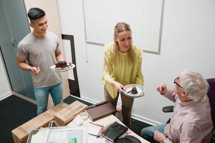 A colleague offering a slice of cake to a coworker at their desk, a small and genuine act that captures what real-life empathy examples look like at work.