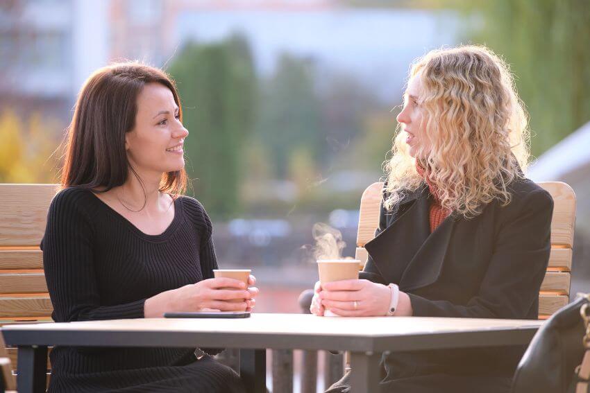 Two women sitting across from each other over coffee, the kind of open and honest conversation that shows how to build trust in a relationship naturally.