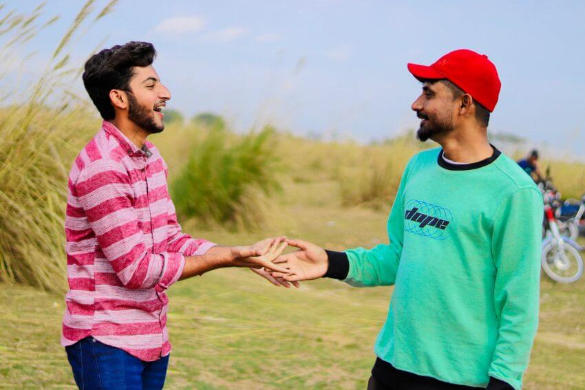 Two men laughing and reaching toward each other outdoors, the kind of easy connection that grows from mutual respect.