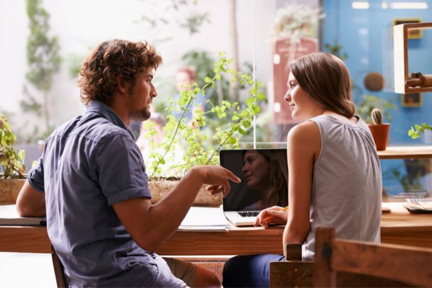 A man and woman talking over a laptop in a plant-filled cafe, the kind of honest conversation that happens when you surround yourself with good people.