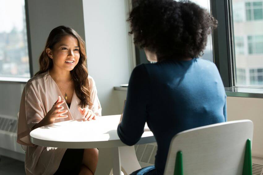Two women at a table in open and engaged conversation, showing mutual respect through the simple act of listening.