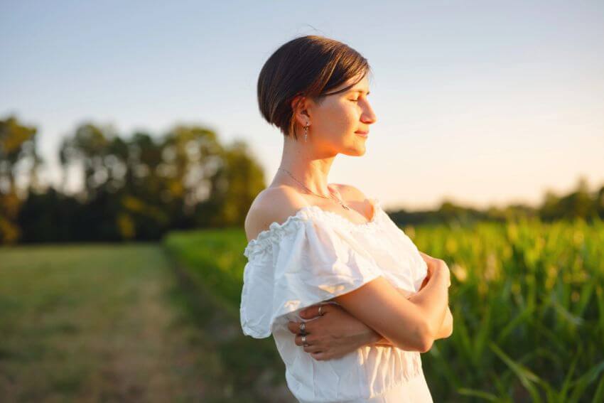A woman standing in a golden field with her eyes closed and face lifted to the light, the kind of still, present moment attentional positivity points you toward.