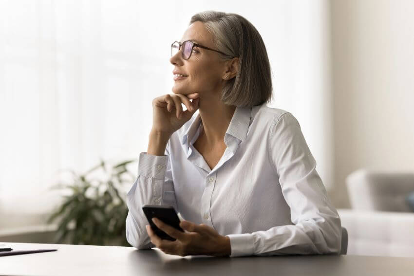 A woman holding her phone while looking away with a calm smile, the half-second pause where attentional positivity begins and the scroll can wait.