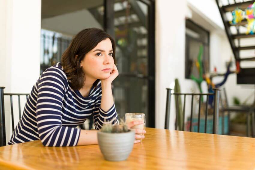 A woman sitting alone at a table with a drink, looking away in quiet thought, the kind of moment that often follows when trust in a relationship has been broken.