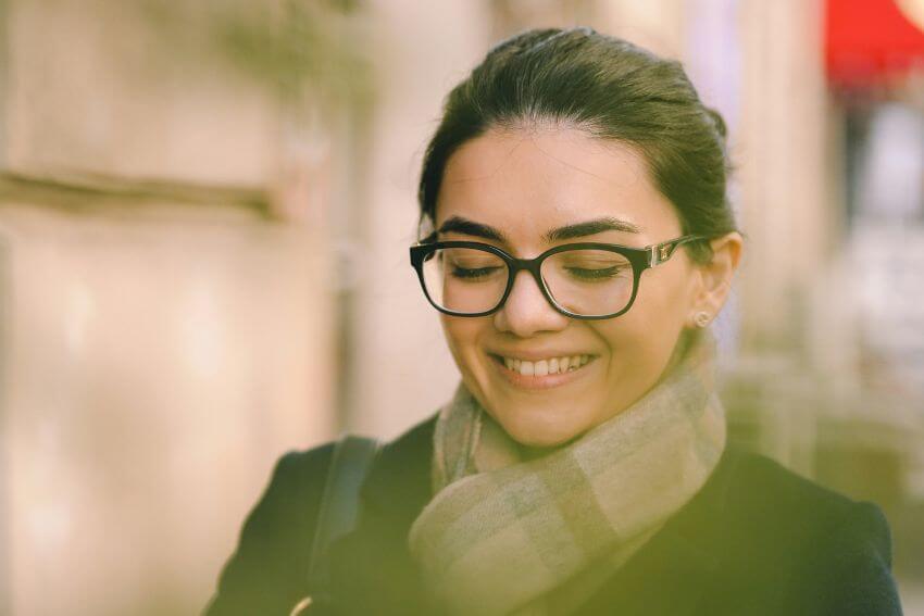 A woman smiling softly to herself outdoors, carrying a quiet sense of inner confidence.