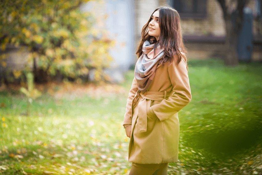 A woman walking through an autumn park with a soft smile, still open, still warm — exactly what it looks like to keep caring too much in the right direction.