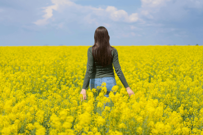A woman walking through in a field of blossoming yellow flowers, what it looks like when caring too much finally lands somewhere worthy of it.